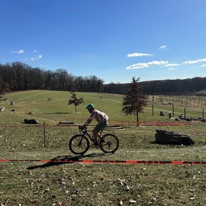 Cyclist riding across open green fields during a mountain bike race.